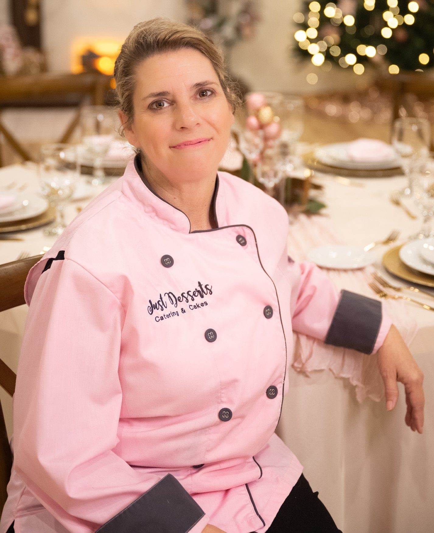 Theresa in her pink Just Desserts chef coat beside a styled holiday table